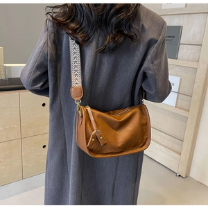 Borsa a tracolla vintage marrone con cinturino etnico e nappina, indossata su giacca grigia