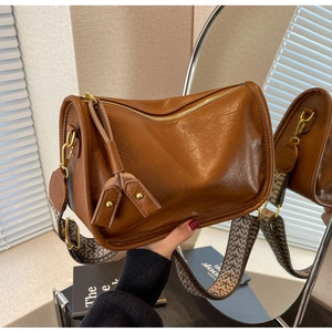 Dettaglio borsa a bauletto in pelle marrone con tracolla geometrica e zip con nappina