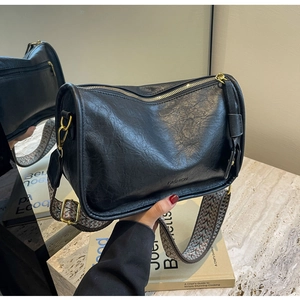 Dettaglio borsa a cuscino in pelle nera con tracolla jacquard e finiture oro