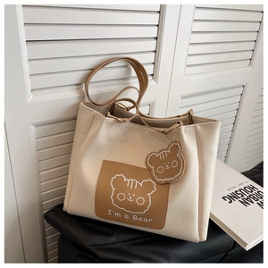 Detail of off-white tote bag with bear print pocket and matching bear charm accessory