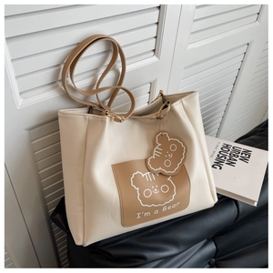 Close-up of cream tote bag featuring a cute cartoon bear print and matching charm accessory