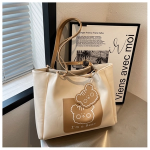 Detail of cream tote bag featuring brown bear pocket and matching leather charm