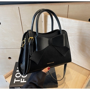 Detail of black leather handbag featuring a large decorative bow and gold zipper accents