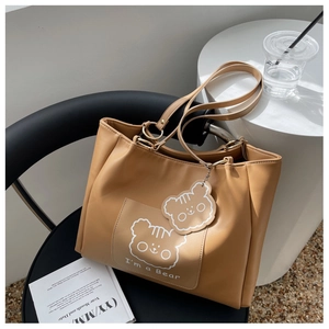 Detail of camel brown leather tote featuring minimalist bear illustration and pendant