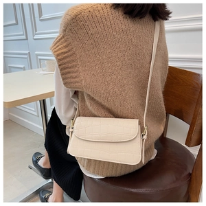 Close-up of off-white crocodile-embossed crossbody bag worn by a model in a cozy cafe setting