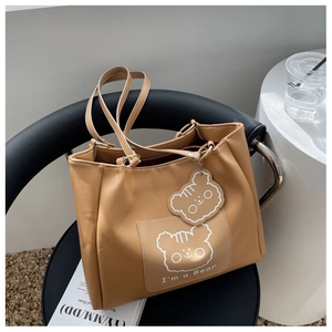 Detail of camel tote bag featuring cute cartoon bear print and matching bear charm