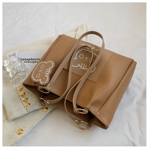 Detail of a large brown faux leather tote bag with white cartoon bear print and charm