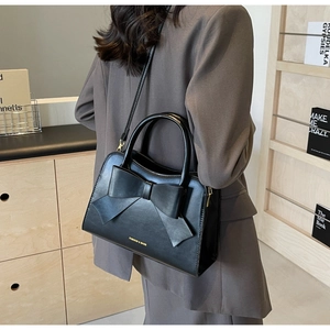 Detail of black leather handbag with oversized bow decoration and golden zipper accent