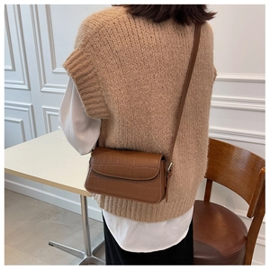 Rear view of model wearing a brown faux crocodile texture crossbody bag in a modern room