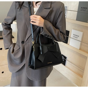 Detail of black glossy handbag featuring a large bow decoration and golden metal hardware