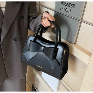 Detailed view of a black structured leather handbag with a large bow and gold zipper