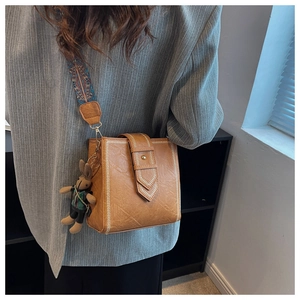 Detail der braunen Eimer-Tasche mit besticktem Gurt und niedlichem Hasenanhänger