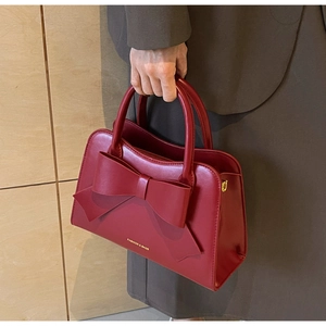 Macro detail of wine red bridal handbag featuring a large bow and gold logo text