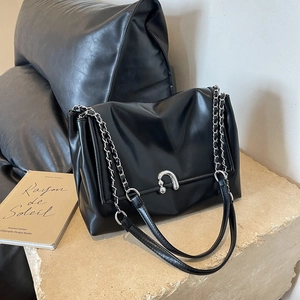 Minimalist black leather underarm bag with silver horseshoe buckle and chain strap on stone