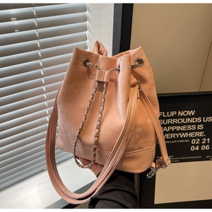 Pink drawstring bucket bag with chain detail held against a stylish home background