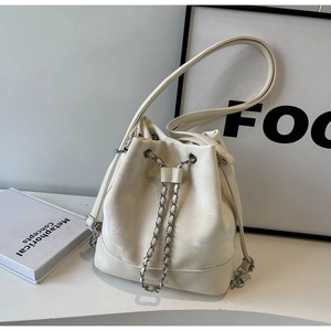 Detailed macro view of the cream bucket bag's drawstring with metal chain and faux leather