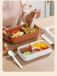 Close-up of compartmentalized bento box with pasta and fruit, including fork and spoon