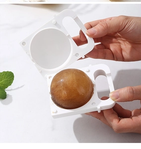 Opening a white silicone ice ball maker to reveal frozen coffee ice spheres