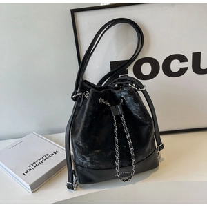 Detail of black drawstring bucket bag with metal chain strap and brand logo bottom