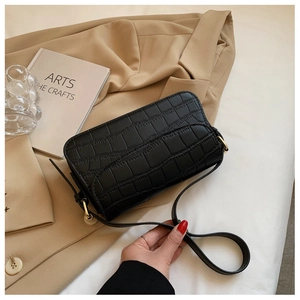Detail of black crocodile texture shoulder bag with gold clasp on a beige blazer background