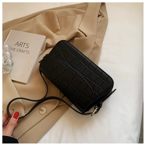 Close-up of black crocodile pattern faux leather shoulder bag on a beige blazer