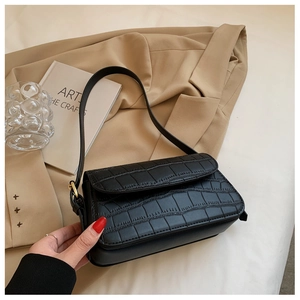 Detail of black crocodile pattern baguette bag with flap closure and metallic hardware