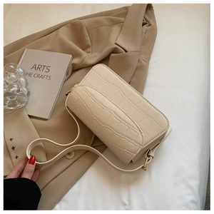 Detail of creamy white crocodile embossed underarm bag with metal buckle on white fabric