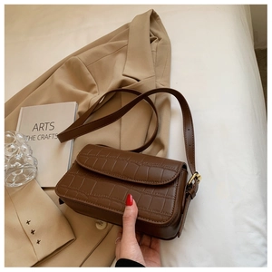Detail of dark brown crocodile pattern texture on a minimalist shoulder bag with gold buckle