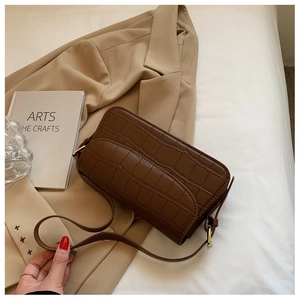 Close-up of brown crocodile texture shoulder bag on a beige blazer background