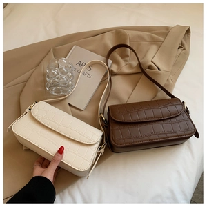 Detail of elegant crocodile-patterned baguette bags in cream and dark brown with gold hardware