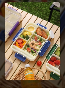 Outdoor picnic scene showing a 5-compartment lunch box with secure snaps and fresh food