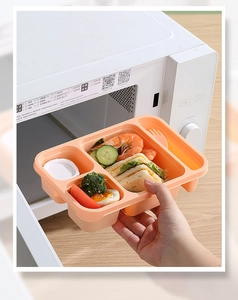 Divided plastic lunch box set with utensils being placed into a microwave oven