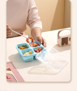 Detail showing a four-compartment lunch box with shrimp and eggs in a cozy home setting
