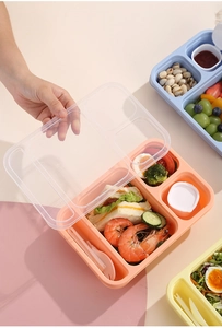 Top view of multi-compartment lunch box with utensils filled with fresh food and snacks