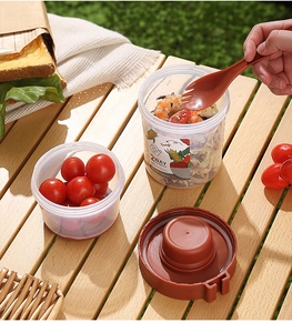 Outdoor picnic scene showing a 560ml+310ml dual-layer salad cup with fork and spoon