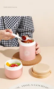 Pink portable double-layer insulated soup cup with a white folding spoon on a beige table