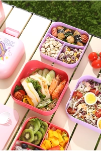 Outdoor picnic scene showing colorful double-layer bento boxes with unicorn patterns