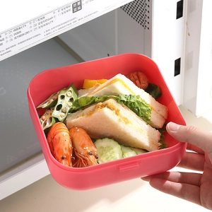 Red double-layer microwaveable lunch box with bento meal shown in front of microwave