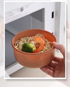 Close-up of a double-layer round bento box with shrimp noodles by a microwave oven