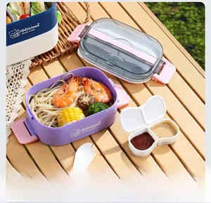 Detail of multi-layer oval bento box with sauce container and fork on picnic table