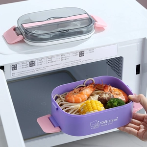Oval bento lunch box with food compartments being placed into a white microwave
