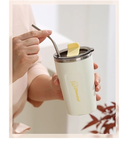 Close-up of cream stainless steel coffee mug with yellow cat pattern and metal straw
