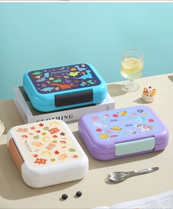 Three children's lunch boxes with dinosaur and unicorn themes on a lifestyle background