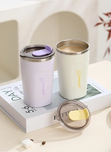 Detail of matte stainless steel coffee mugs with cat illustrations and clear lids on a desk