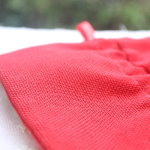 Red exfoliating bath glove made of coarse textured fiber with a convenient hanging loop