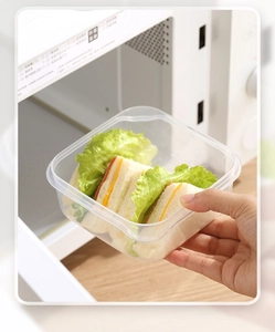 Clear microwave-safe plastic food container being used for heating a sandwich