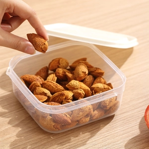 Transparent food storage container with white lid filled with almonds on wooden table