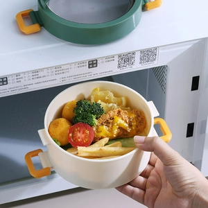 Cream white round portable lunch box with yellow handle shown in front of a microwave