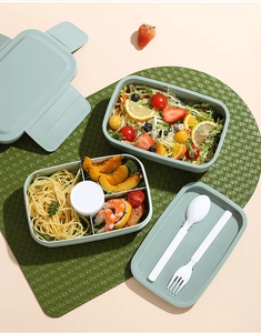 Primer plano de fiambrera bento verde de doble capa con divisores y cubiertos