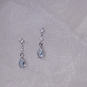 Macro detail of silver drop earrings with light blue pear-cut stones and crystal accents